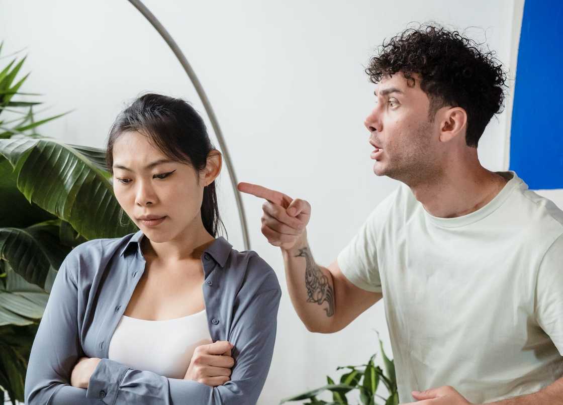 A man argues and points while a woman looks down with folded arms.