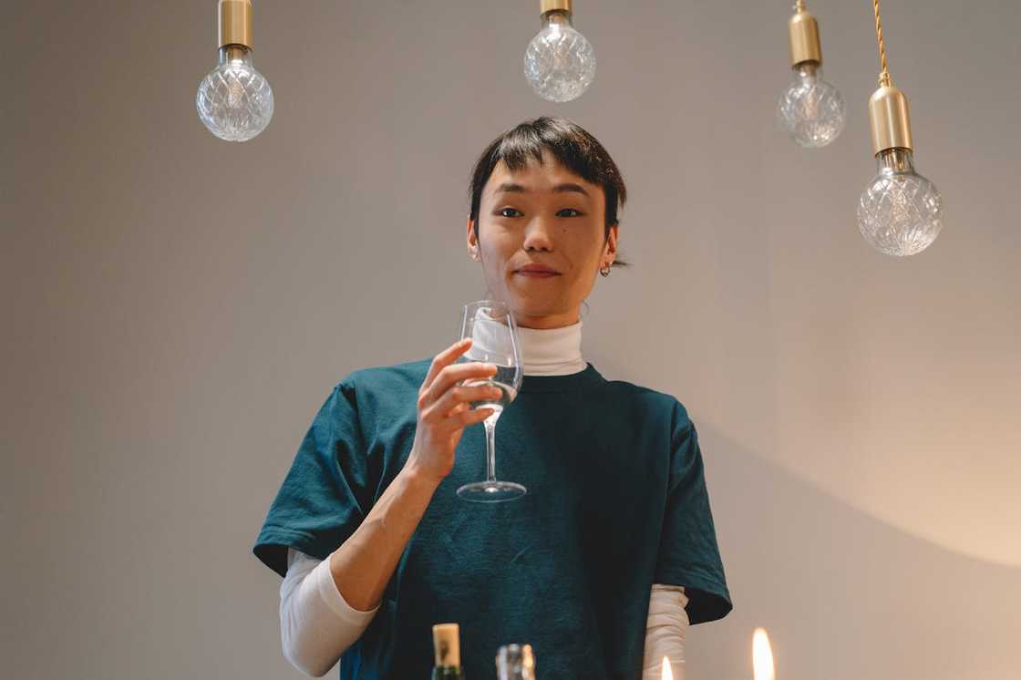 A woman holding a wine glass under hanging pendant lights, smiling gently. A woman holding a wine glass under hanging pendant lights, smiling gently.