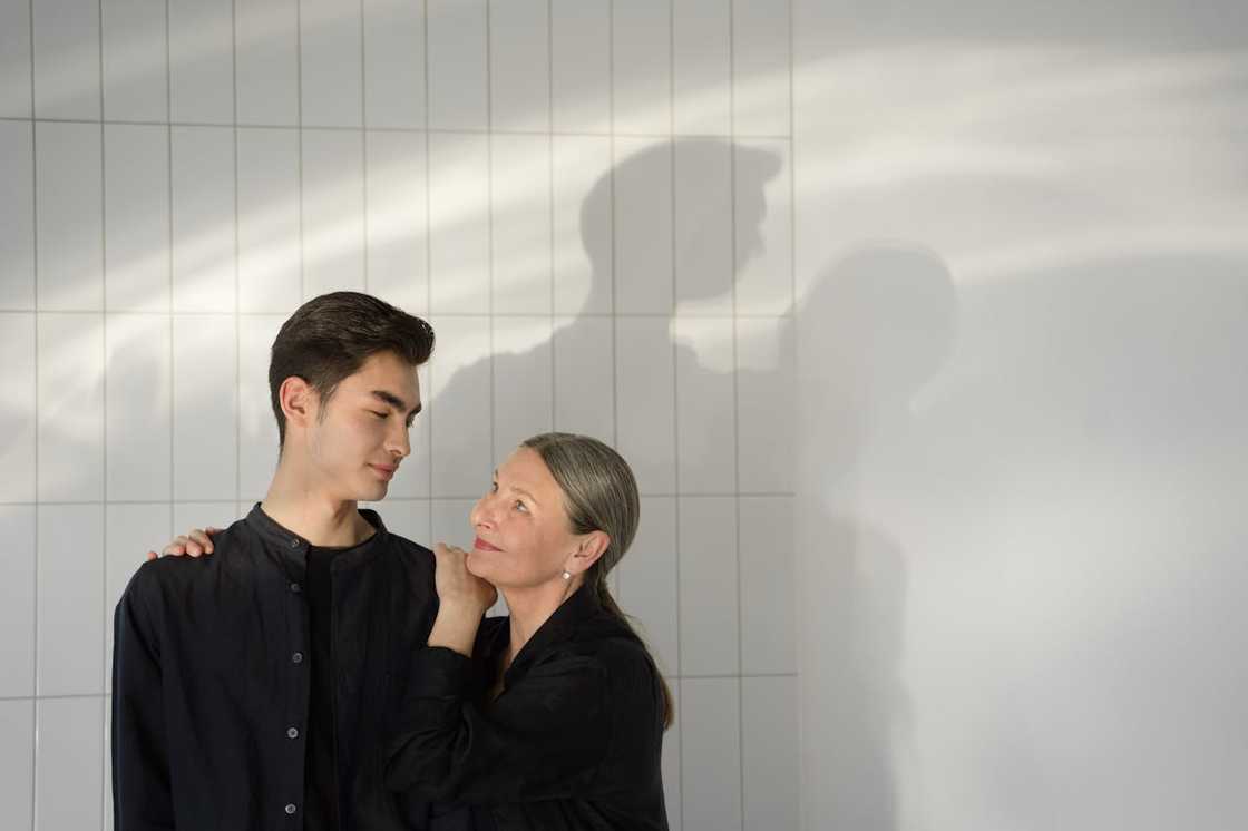 A woman stands close to a young man, resting her hand on his shoulder.