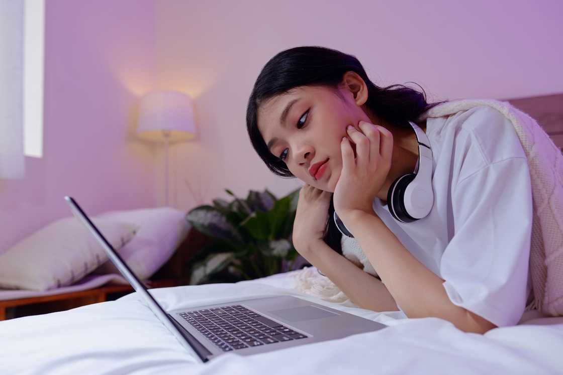 A lady reading from her laptop at night while in bed