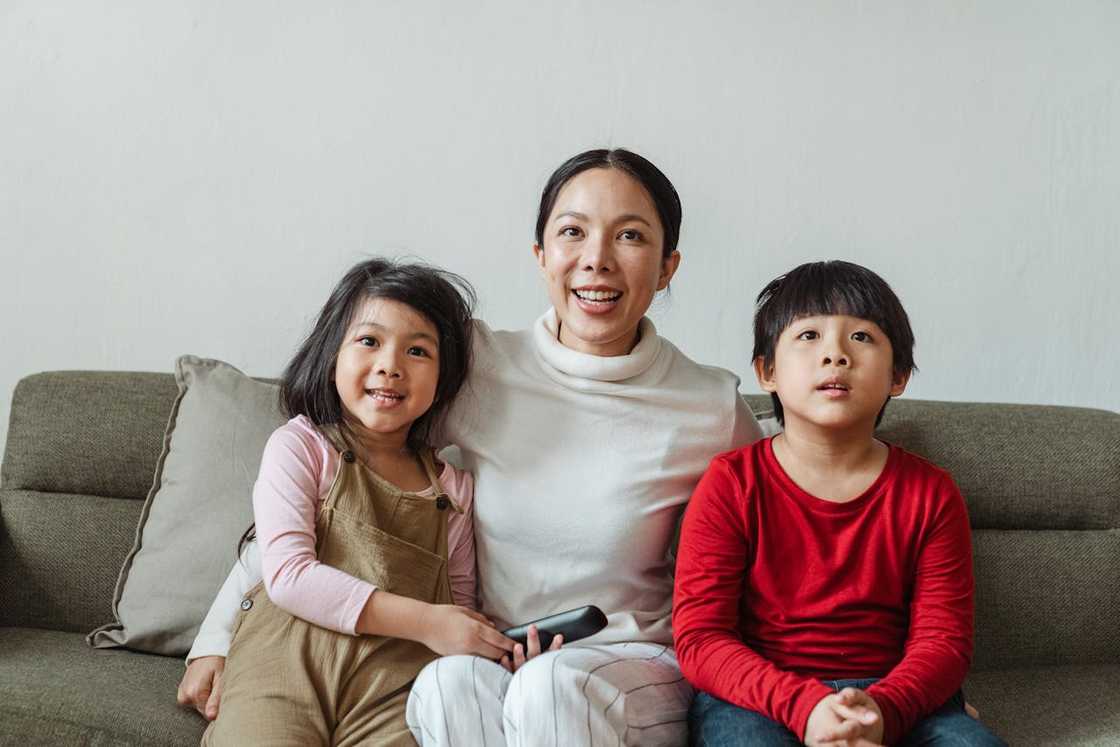 Mother and two children are sitting together on a sofa watching TV. Mother and two children are sitting together on a sofa watching TV.