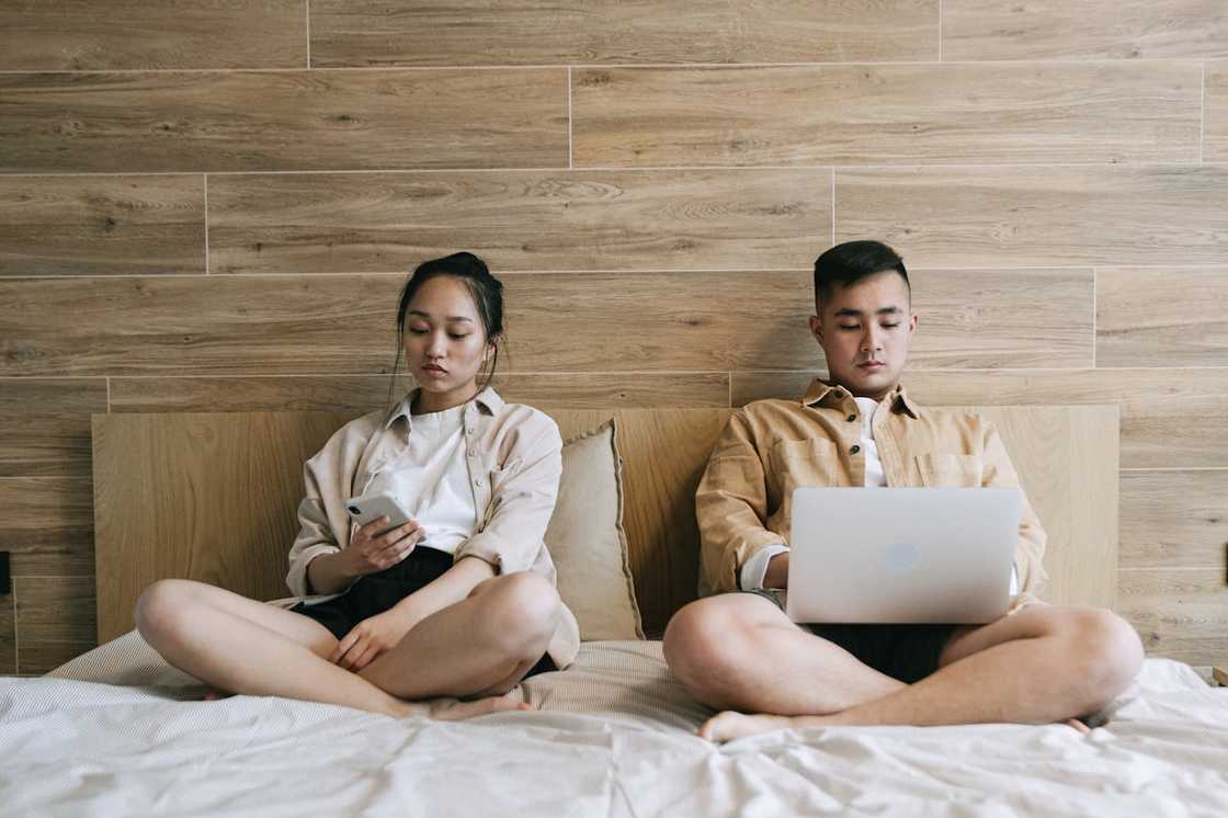 A man and a woman sitting on the bed while using gadgets. A man and a woman sitting on the bed while using gadgets.