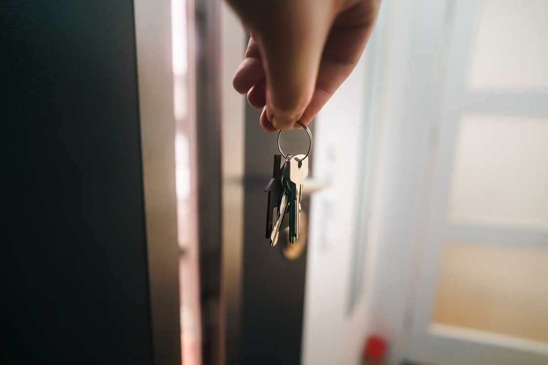 Hand holding a set of house keys near an open door. Hand holding a set of house keys near an open door.