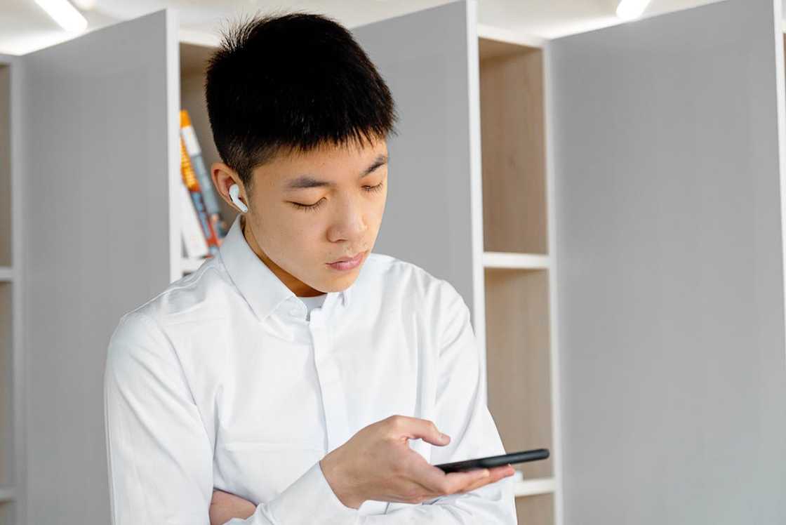 A person in a white shirt looks at a smartphone indoors.