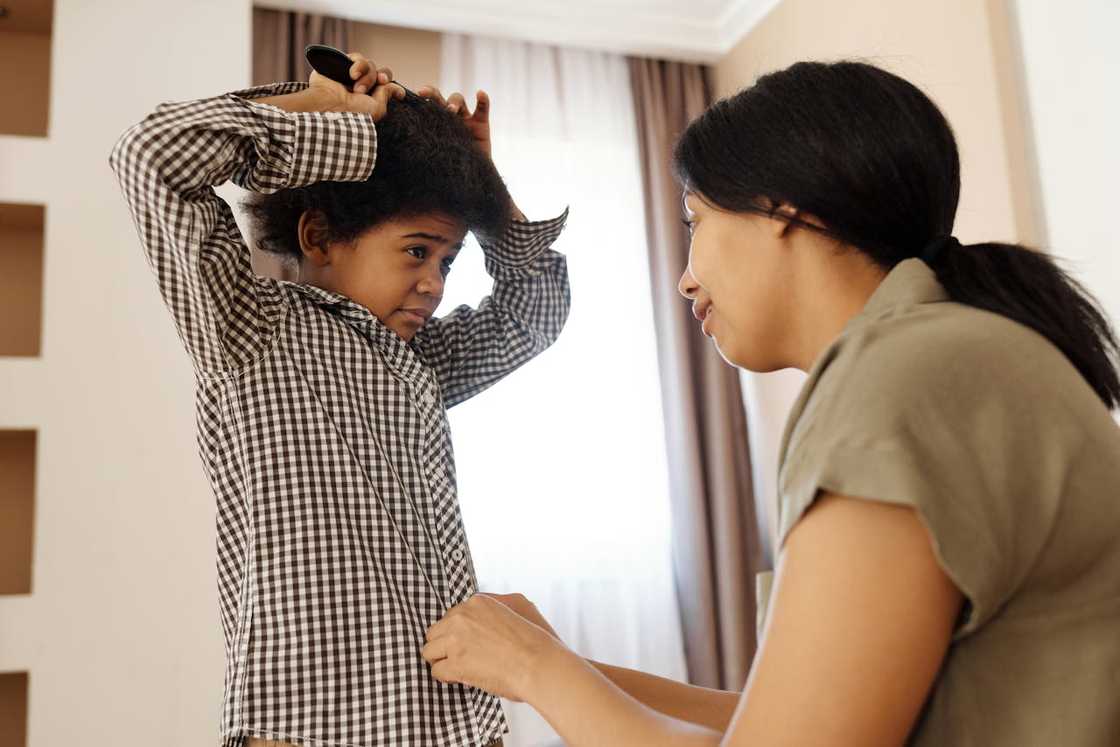A mother helping a young boy comb his hair at home.
