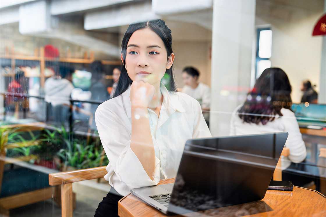 A thoughtful woman works on a laptop