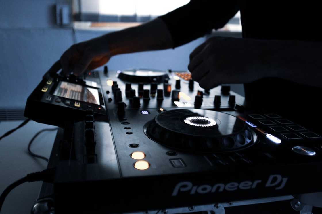 A close-up of a DJ adjusting knobs and buttons on a Pioneer mixer in a dimly lit setting.