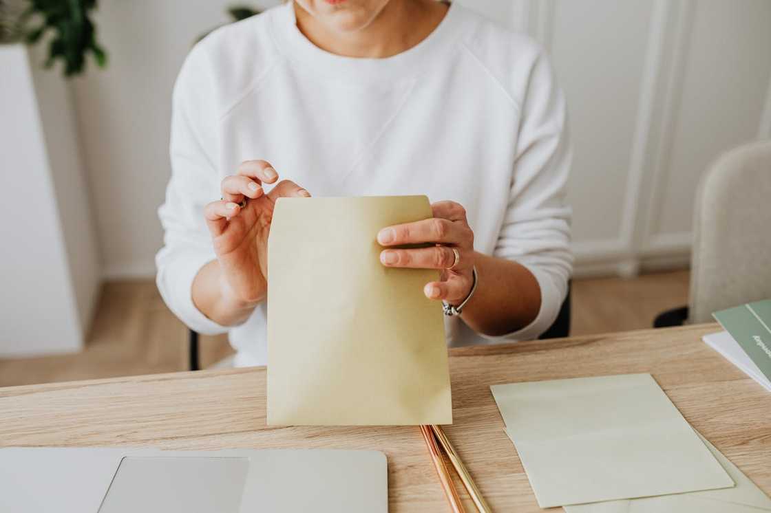 A person sits at a desk holding a brown envelope in both hands. A person sits at a desk holding a brown envelope in both hands.