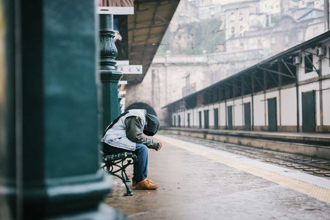 A person sits on a wooden bench at a train station. A person sits on a wooden bench at a train station.