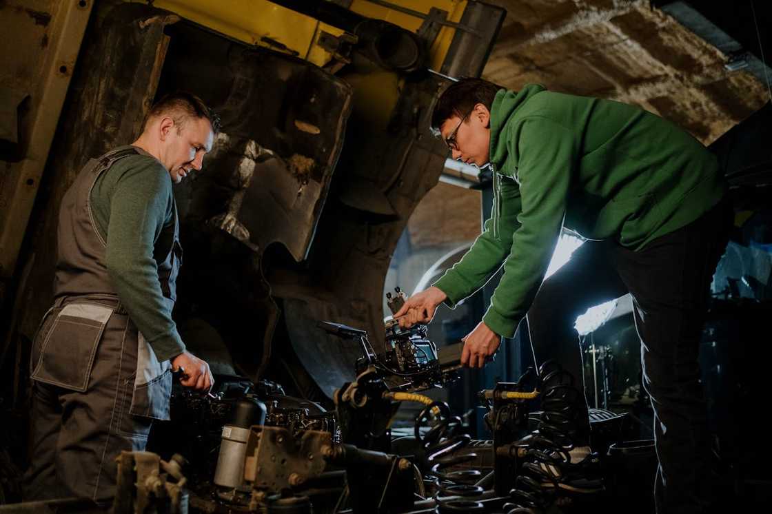 Two mechanics inspect a vehicle's engine with the hood open. Two mechanics inspect a vehicle's engine with the hood open.