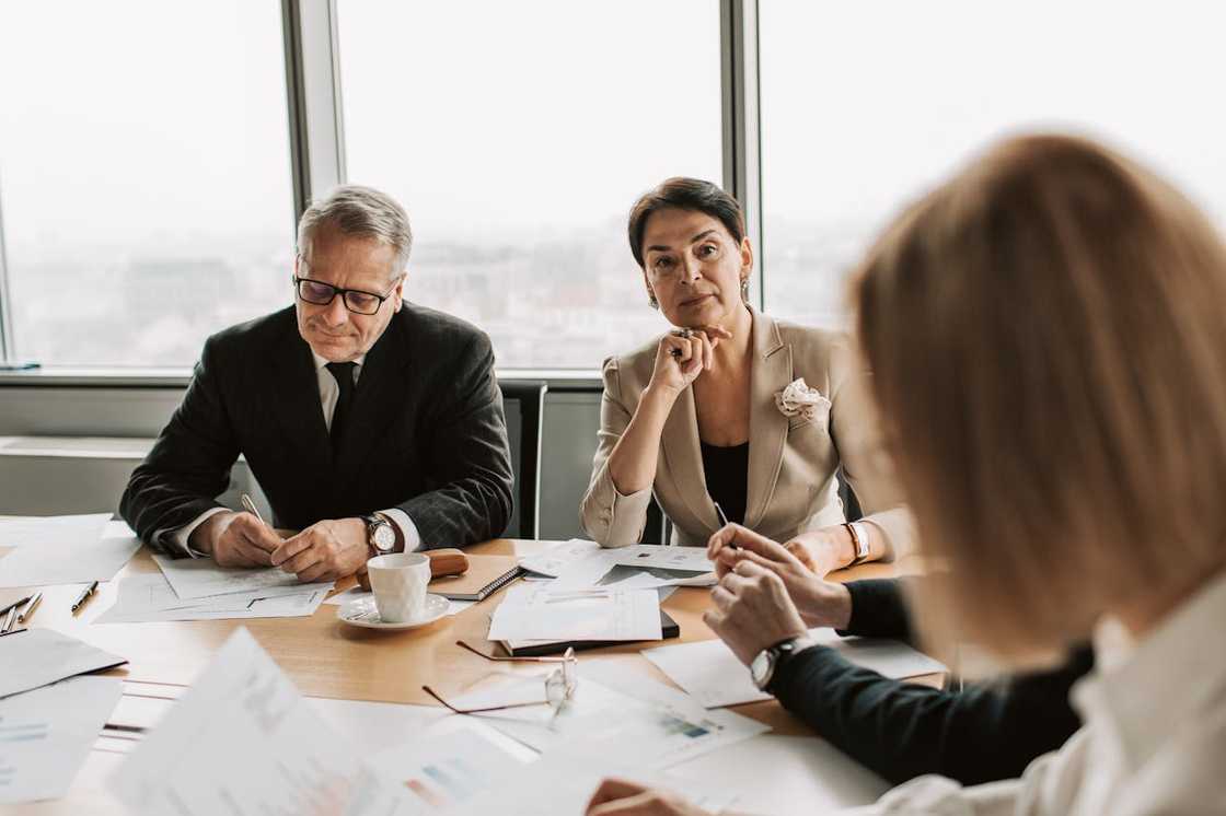 Three adults sit at a table reviewing documents during a meeting.