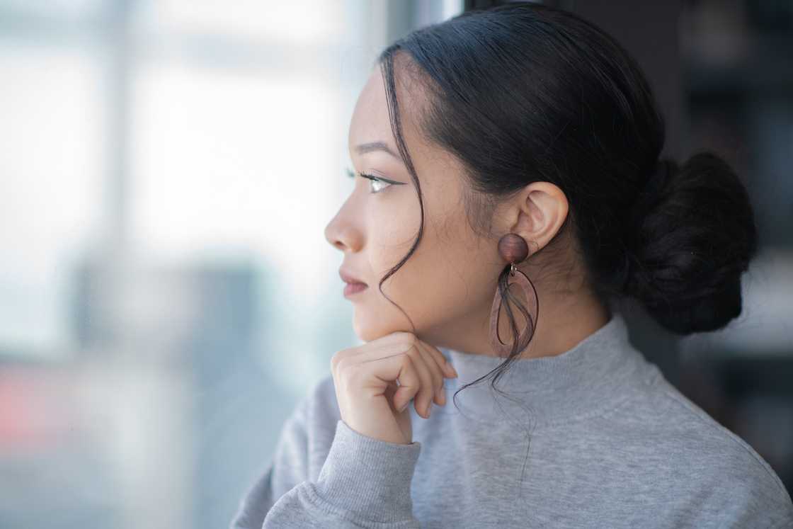 A young woman standing near a window thinking. A young woman standing near a window thinking.