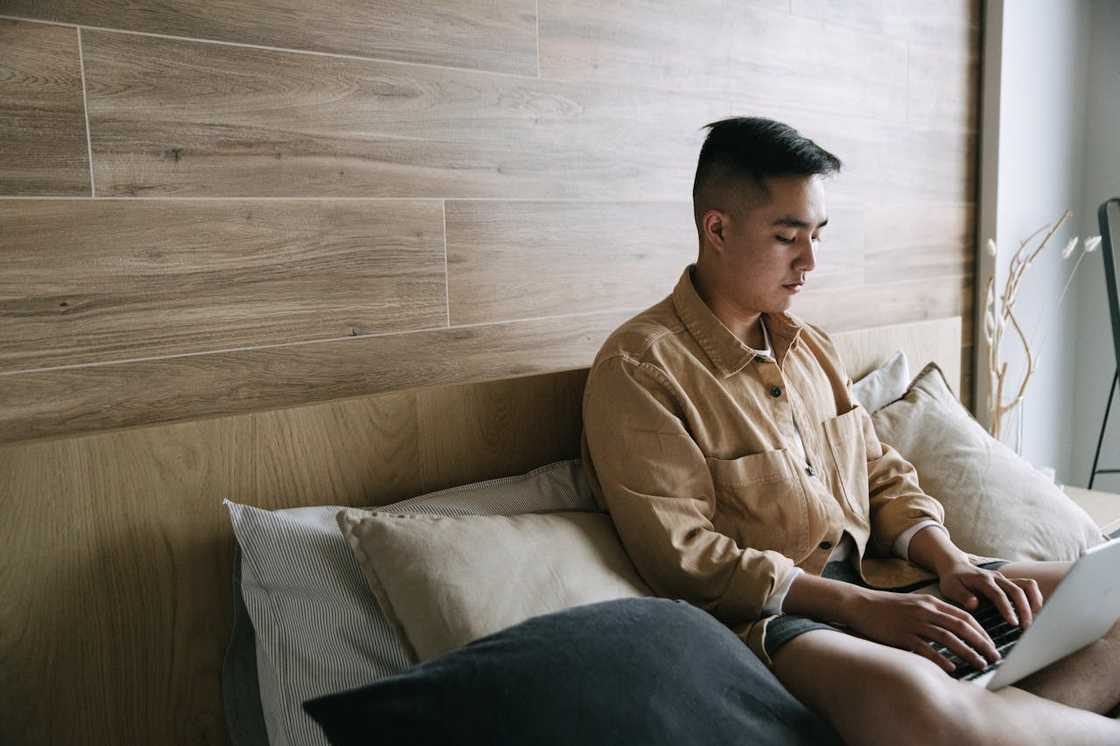 A teenager types quietly on his laptop while on his bed.