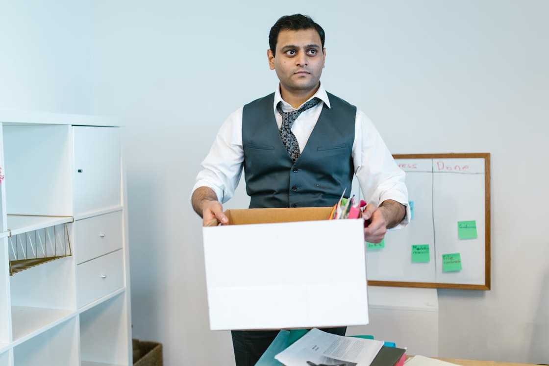 A man holds a box of personal belongings inside an office. A man holds a box of personal belongings inside an office.