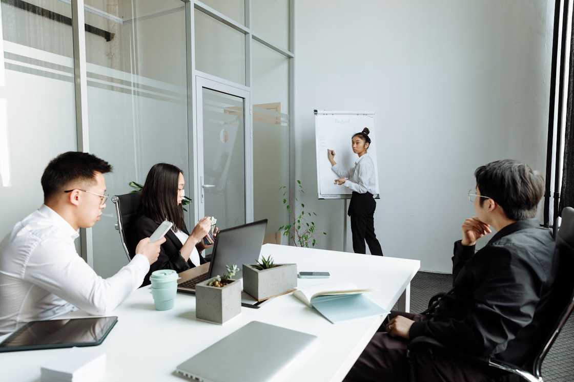 A woman presents at a flip chart around a conference table. A woman presents at a flip chart around a conference table.