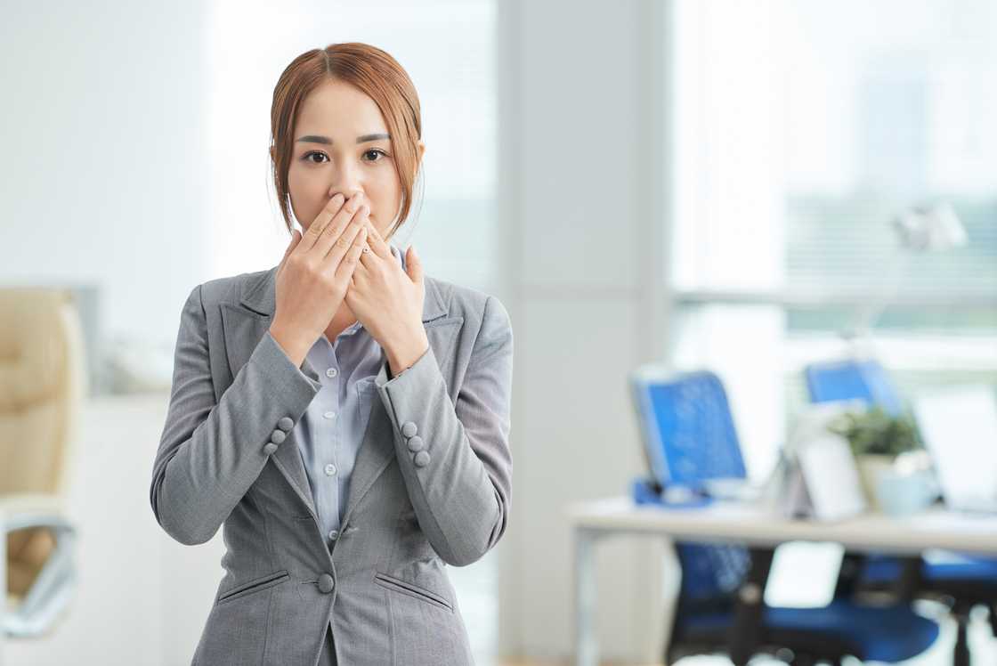 A terrified woman covering her mouth by the hands while standing at office