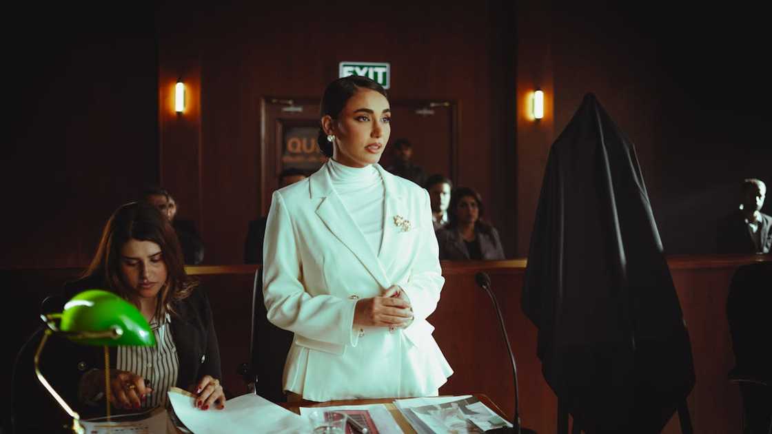 A woman in a white suit stands and testifies in a courtroom.