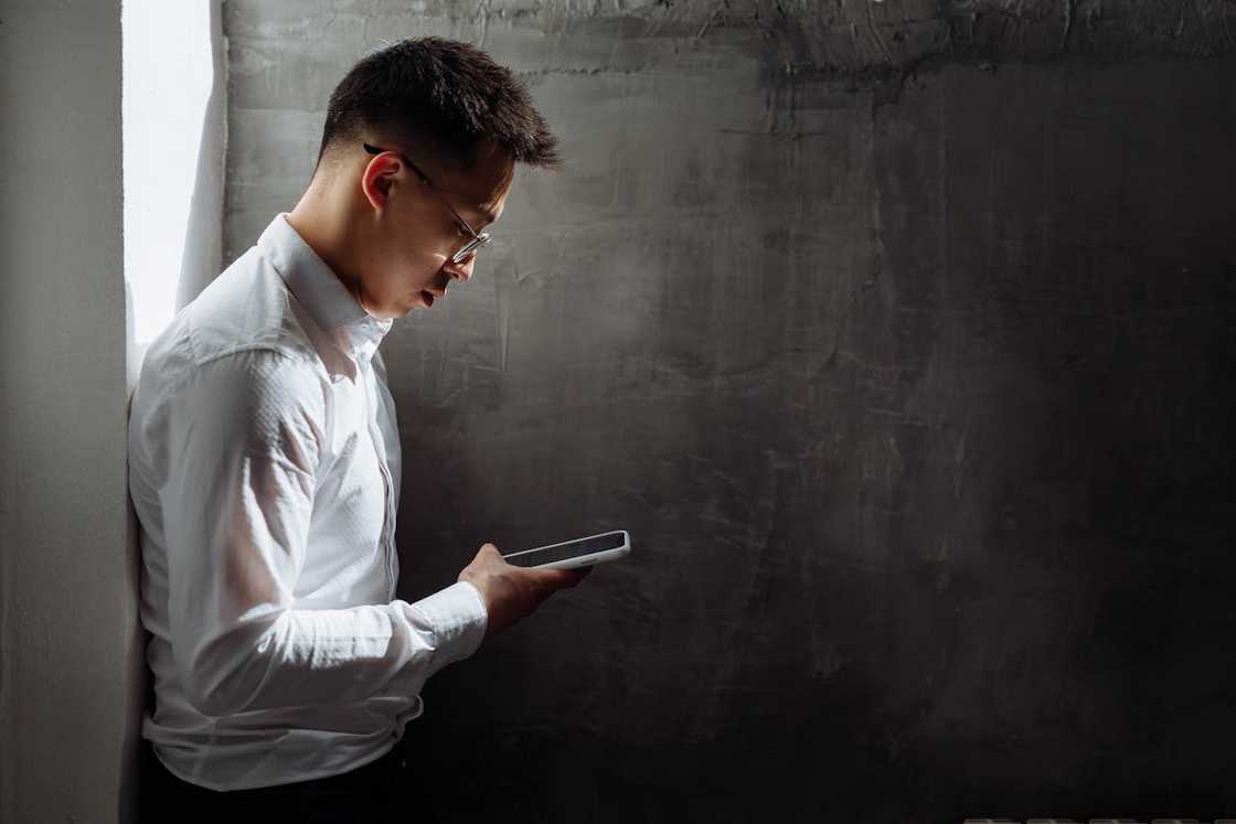 A young man reads a message on his phone in a dimly lit room.