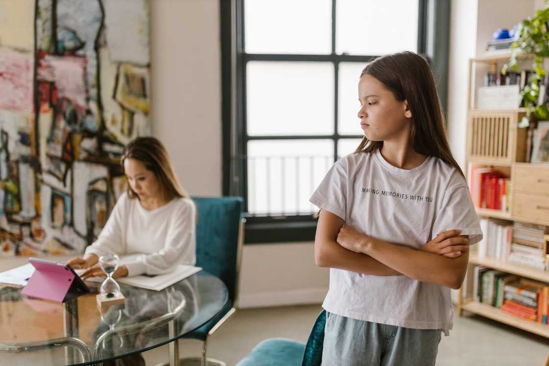 A young girl stands with her arms crossed, looking unhappily away from her mother. A young girl stands with her arms crossed, looking unhappily away from her mother.
