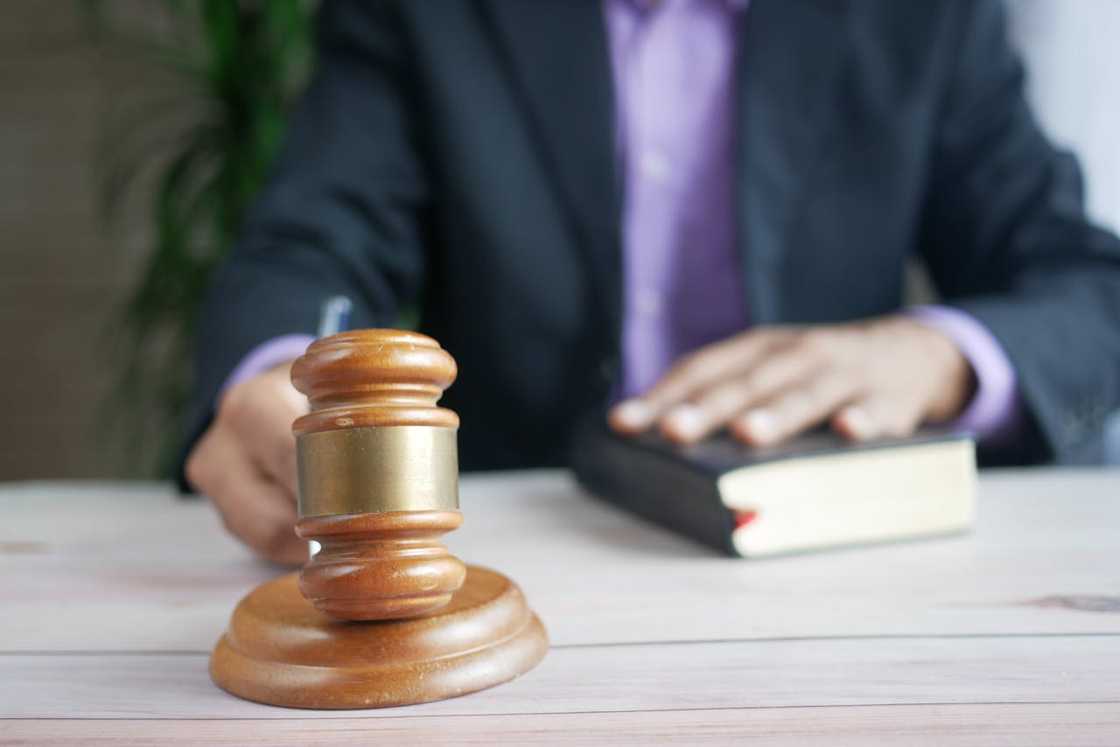 A judge's gavel on a desk with a hand resting on a law book. A judge's gavel on a desk with a hand resting on a law book.