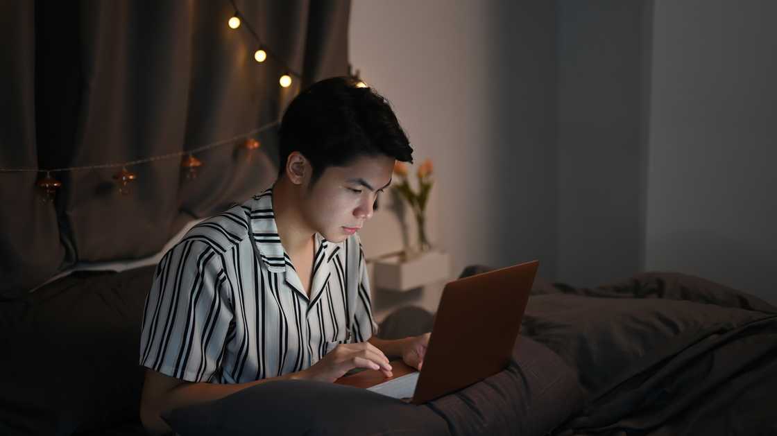 Young man working with computer laptop on his bed at late night. Young man working with computer laptop on his bed at late night.