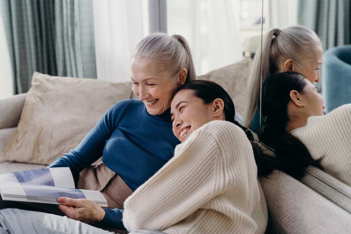 An older woman and a younger woman sit close together on a couch. An older woman and a younger woman sit close together on a couch.