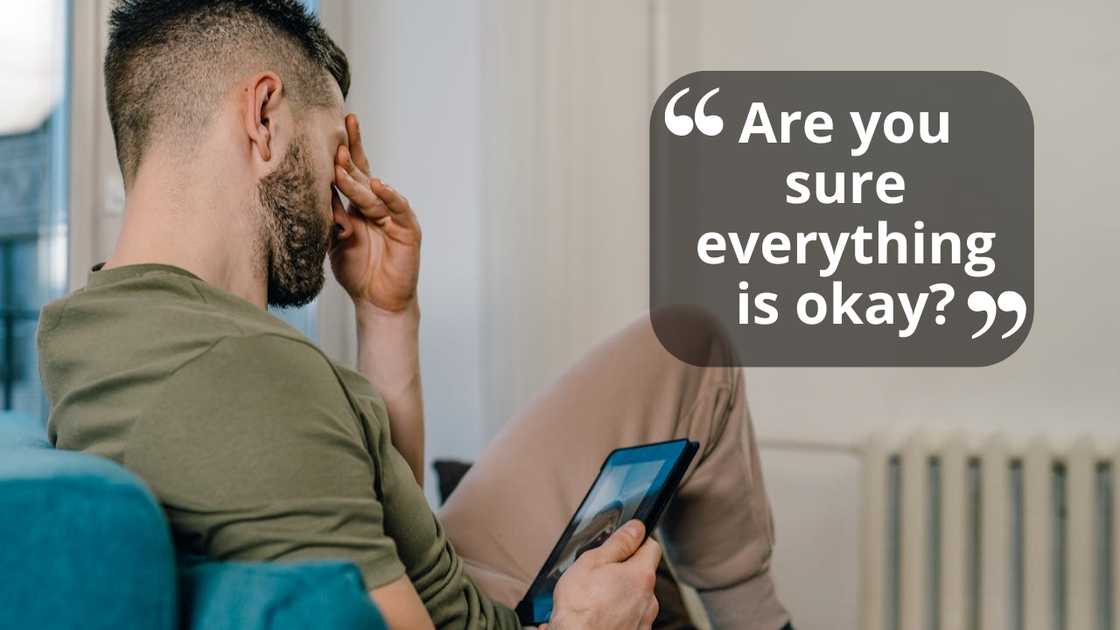 A man sits on a sofa holding a tablet and covering his face with his hand in distress. A man sits on a sofa holding a tablet and covering his face with his hand in distress.