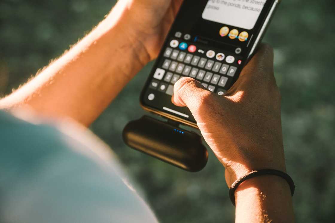 A person holds a phone while typing a message outdoors.