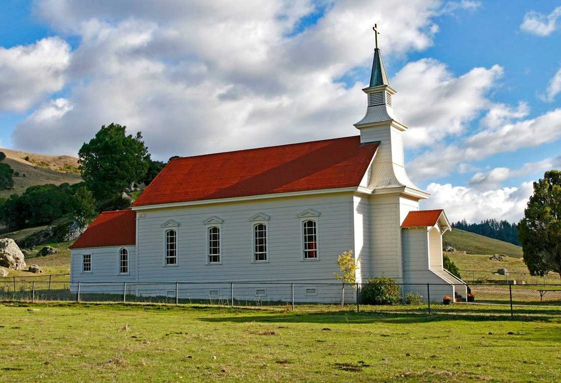 Small white church with a red roof standing in a grassy rural field.