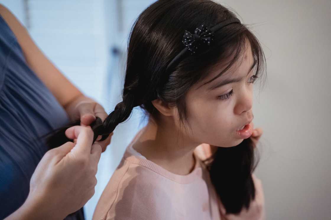An adult styling a child’s hair while the child sits calmly. An adult styling a child’s hair while the child sits calmly.