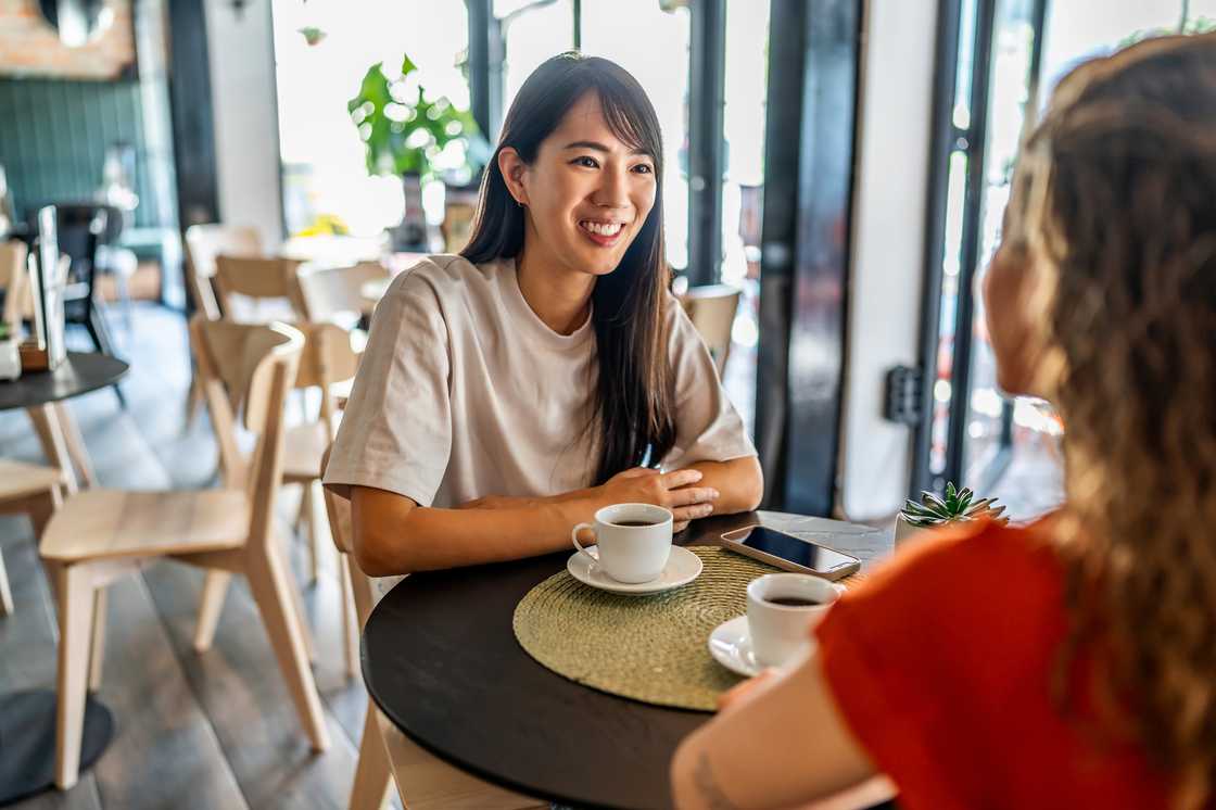 Two young women engaging in lively conversation while sipping coffee together in a cozy cafe Two young women engaging in lively conversation while sipping coffee together in a cozy cafe