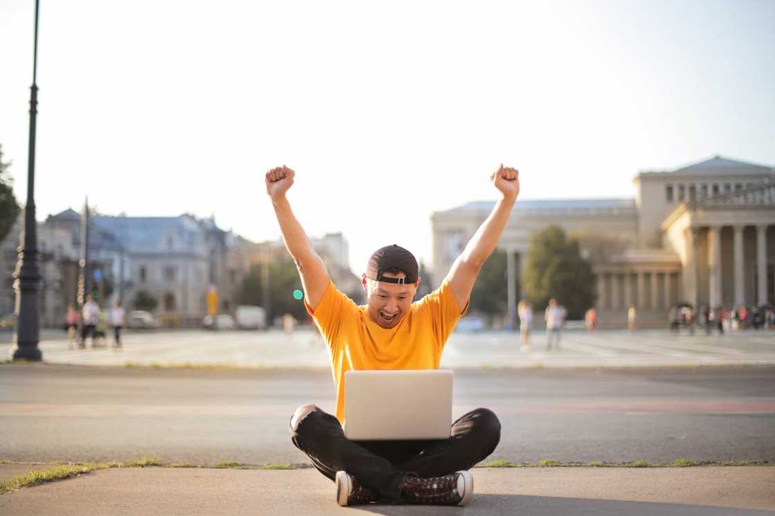 A man sits outdoors with a laptop on his lap.