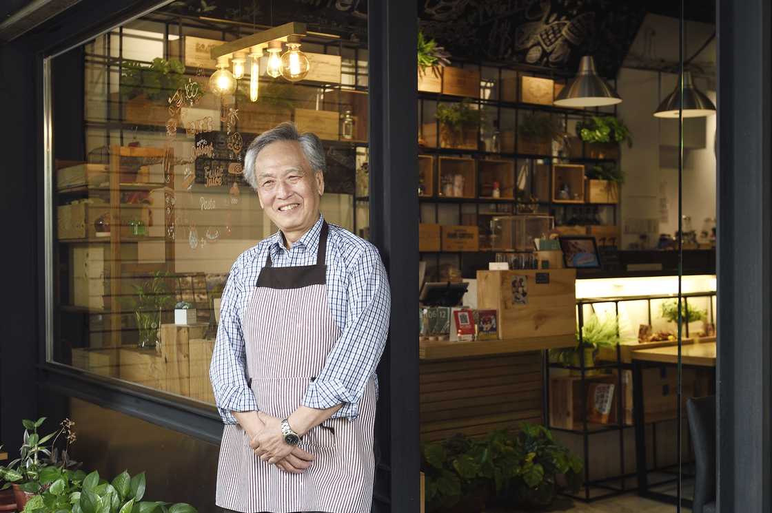 An elderly man is standing outside a cafe
