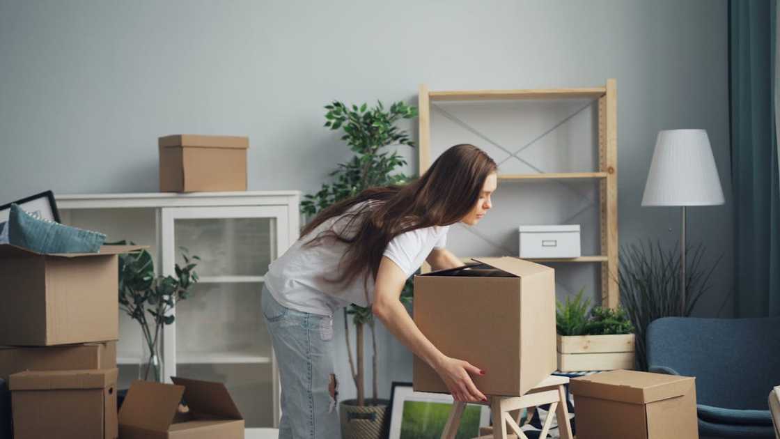 A woman unpacking a cardboard box in a sparsely furnished living room. A woman unpacking a cardboard box in a sparsely furnished living room.