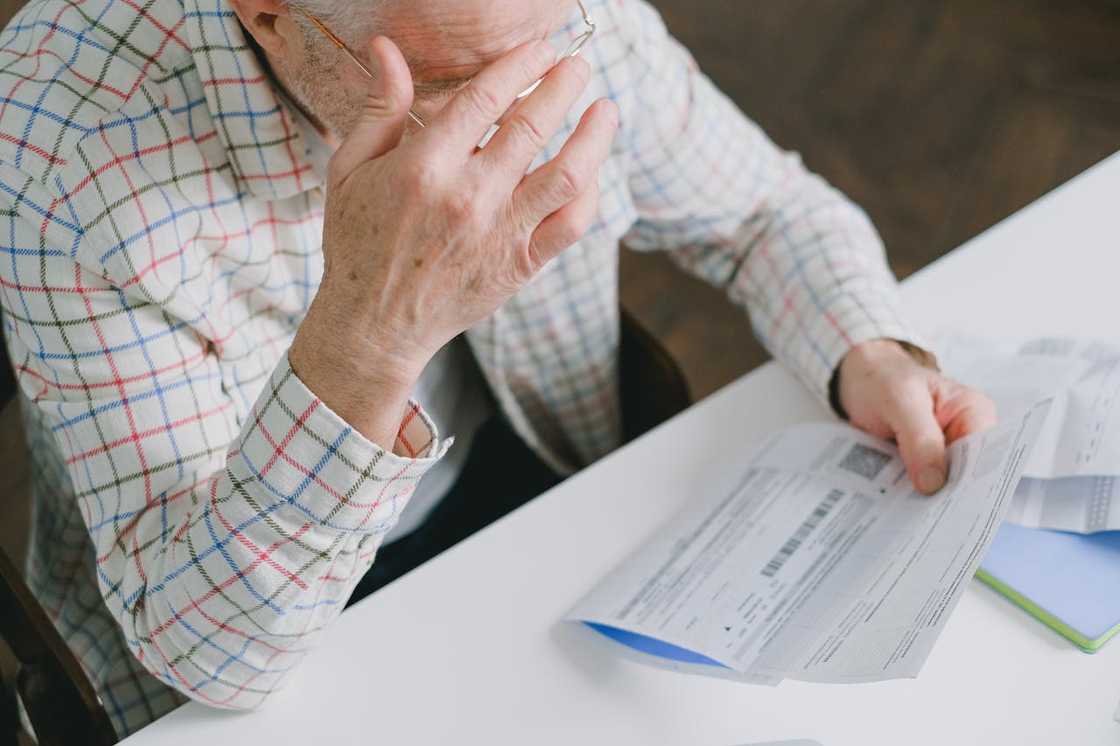 An older man looks stressed while reviewing a document at a desk. An older man looks stressed while reviewing a document at a desk.
