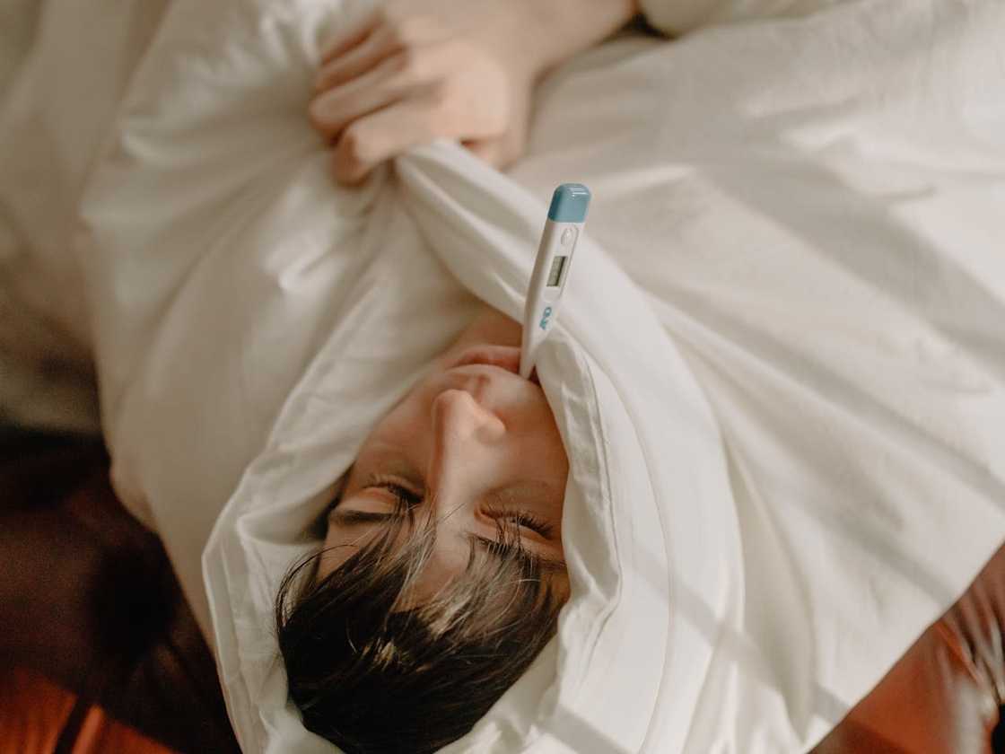 A person resting in bed with a digital thermometer in their mouth. A person resting in bed with a digital thermometer in their mouth.