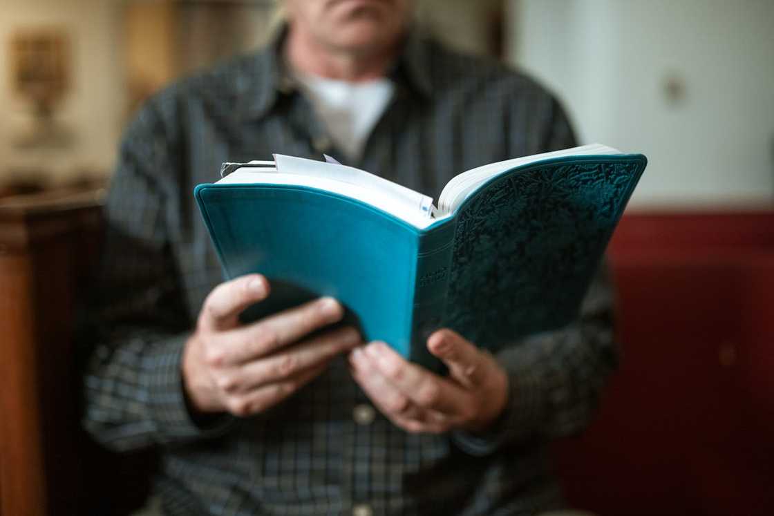 A man holds and reads a bible indoors.