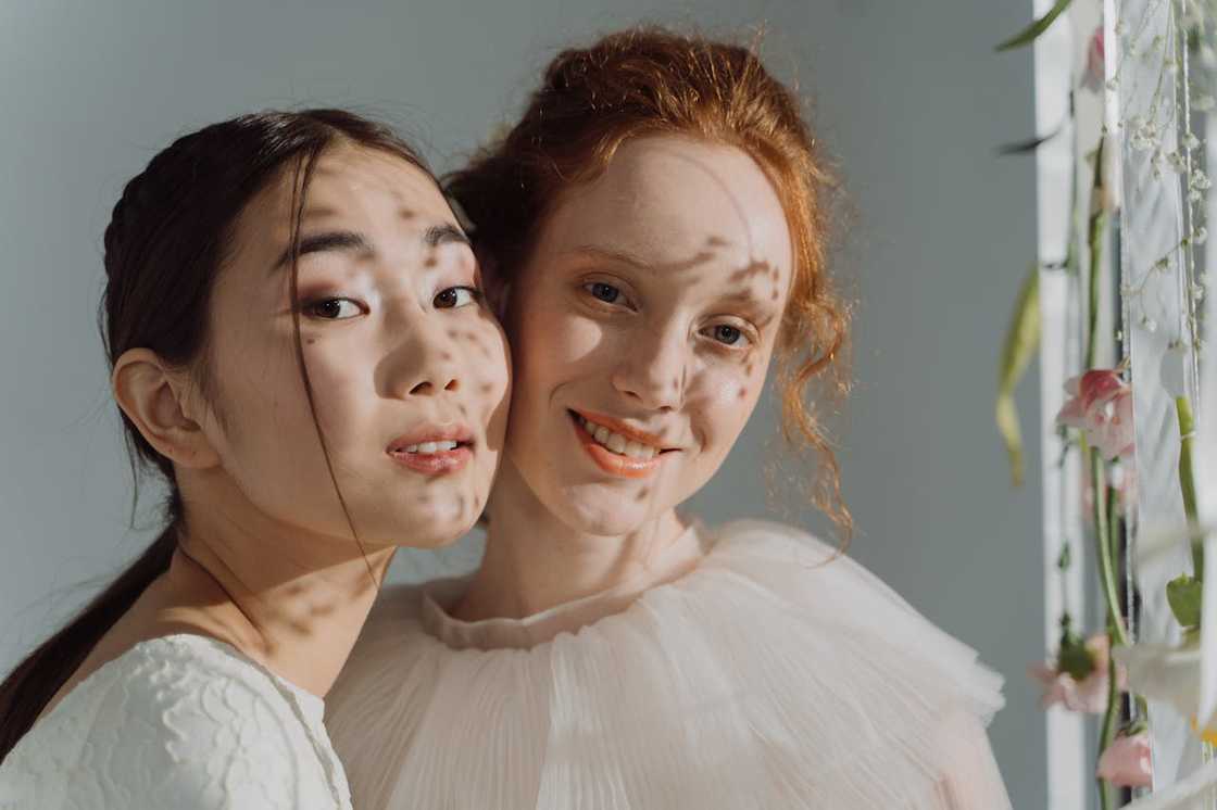 Two women in light dresses smiling closely together in soft natural light.