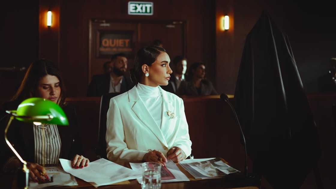 A woman in a white suit is seated at a courtroom desk during a legal proceeding.