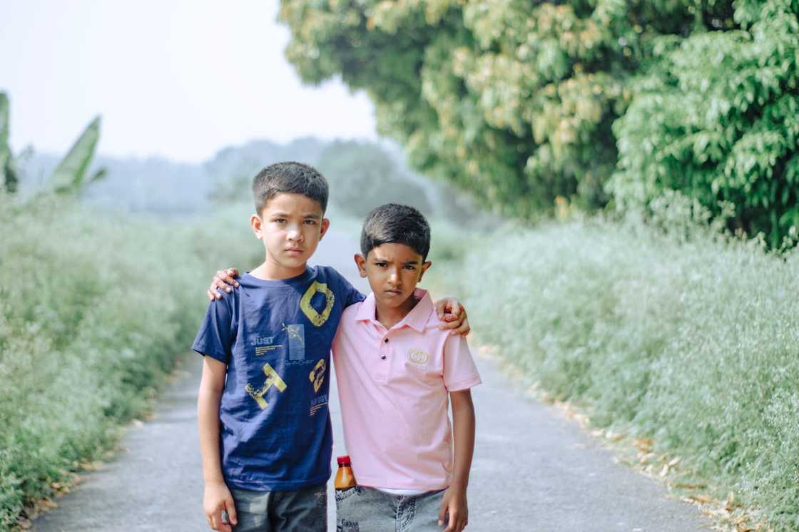 Two children stand side by side, one with an arm around the other. Two children stand side by side, one with an arm around the other.