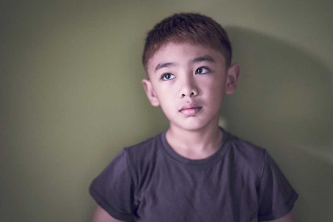 A sad boy leaning against a green wall