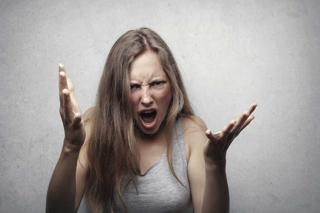 A woman expresses intense anger, shouting with her hands raised in frustration.