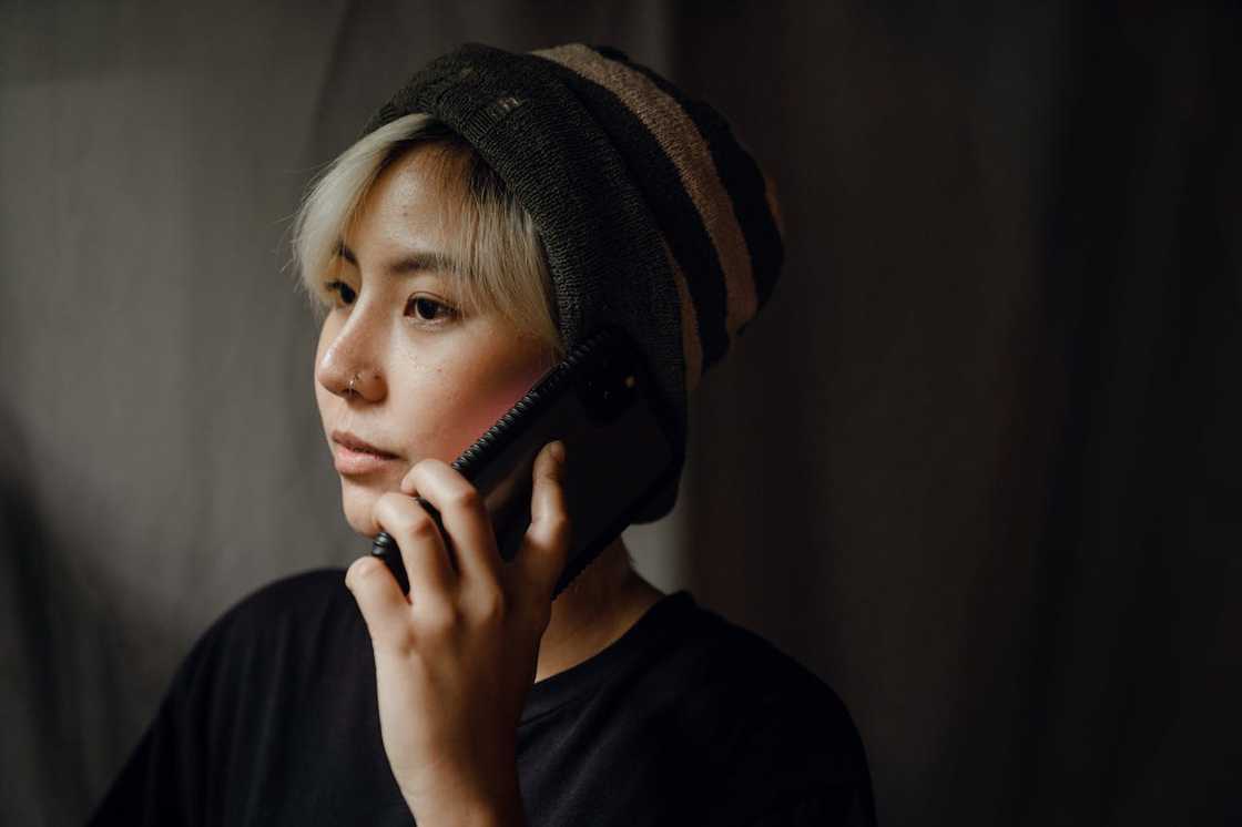 A woman wearing a beanie holds a phone to her ear in low light.