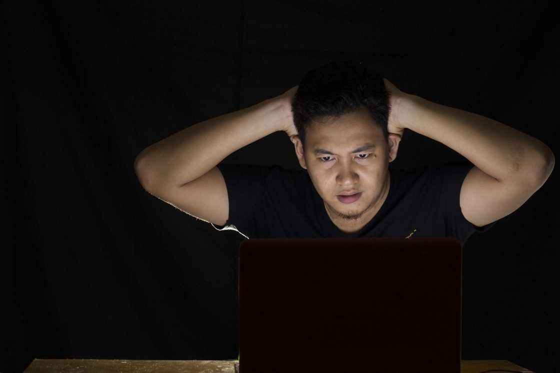 A young man shocked in front of his laptop in the dark A young man shocked in front of his laptop in the dark