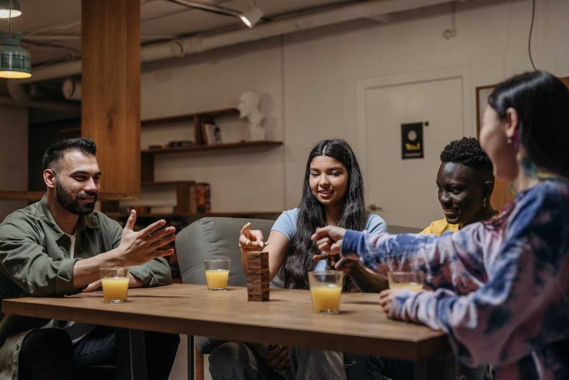 A group of friends sit around a table playing Jenga and drinking juice.