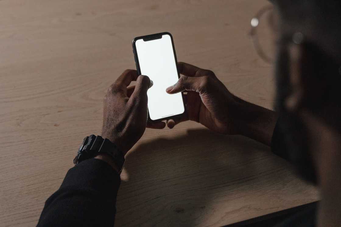A person holds a smartphone with a blank screen while sitting at a table. A person holds a smartphone with a blank screen while sitting at a table.