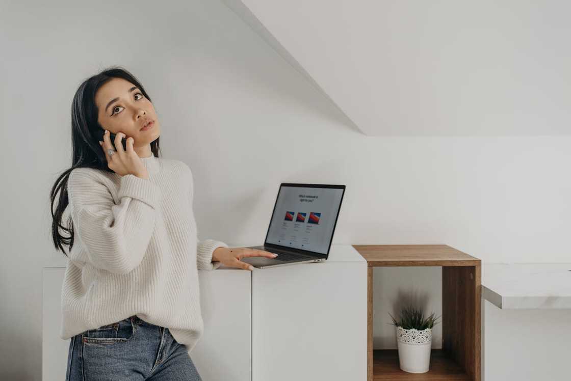 A woman on a call while standing beside a laptop. A woman on a call while standing beside a laptop.