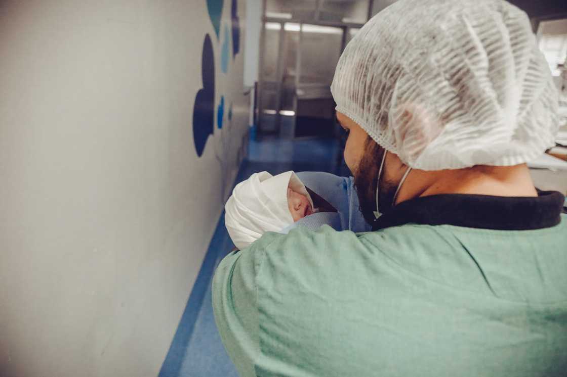 A person in a green medical gown holds a newborn.