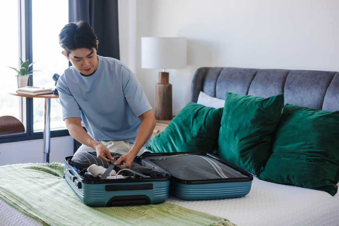 A young man packing his clothes in his bedroom