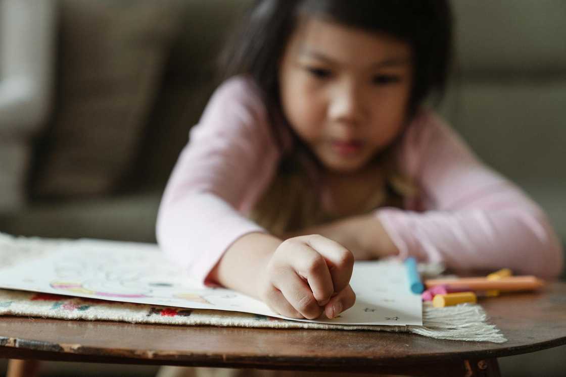 A young girl draws with crayons at a small table. A young girl draws with crayons at a small table.